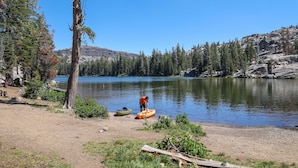 Un lago con kayak y una persona a punto de remar, rodeado de árboles y un cielo despejado.