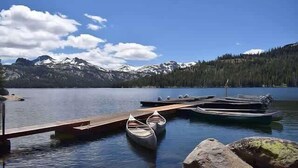 Un lago tranquilo con un muelle, canoas y montañas nevadas al fondo.
