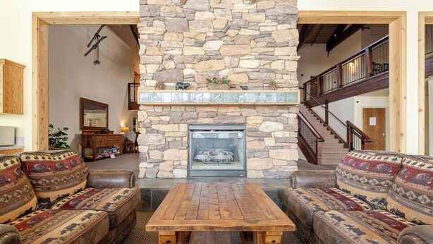Una chimenea de piedra, una mesa de madera y sofás con diseños en una sala de estar.