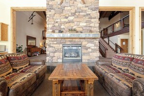 A stone fireplace, wooden table, and patterned sofas in a living room. - The Lookout Loft  Great views and King Sized Bed (Kirkwood)