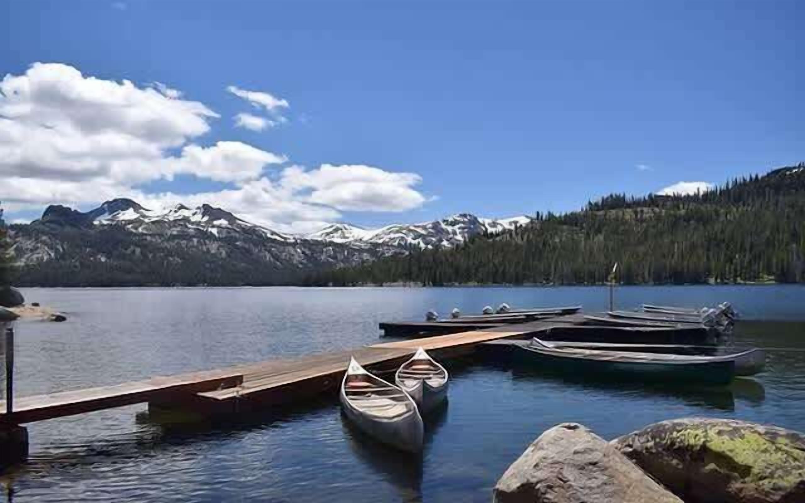 Un lac paisible, avec un quai, des canoës et, au loin, des montagnes aux sommets enneigés.