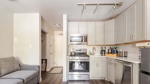 Una cocina moderna con armarios blancos, electrodomésticos de acero inoxidable y un sofá gris en la zona de estar contigua.