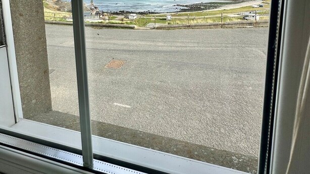 A view from inside a building, looking out through a window at a coastal area with a parking lot and grassy fields.