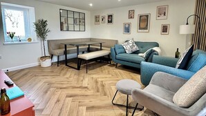 A modern living room with a herringbone floor, a sofa, a chair, a coffee table, a small table with a vase, and a lamp.