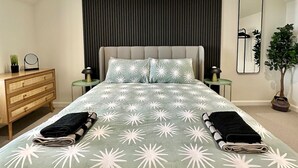 A modern bedroom with a bed, bedside tables, a dresser, a mirror, and a potted plant.