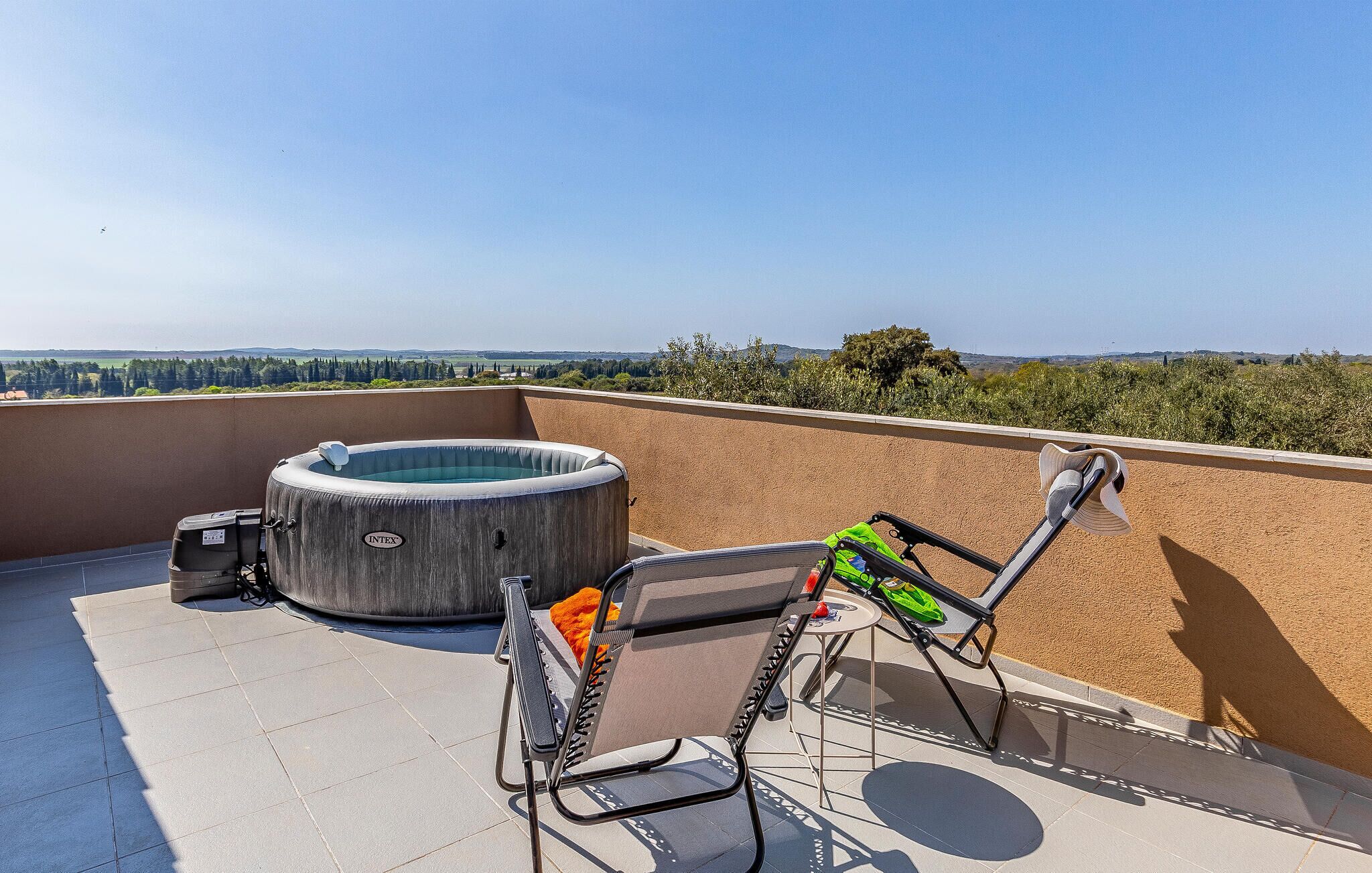 Une terrasse sur le toit avec un jacuzzi, deux chaises et une vue sur la campagne.