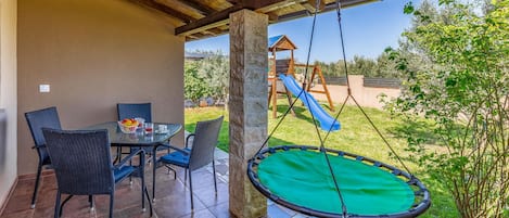 Eine Außenpatio mit Esstisch und Stühlen, einer Schaukel und einer Rutsche im Hintergrund.
