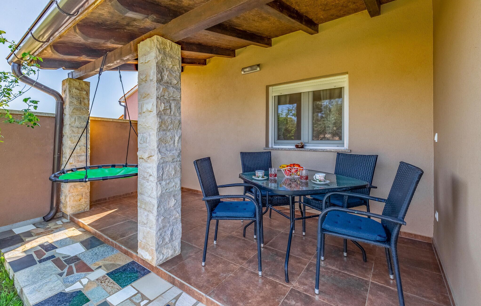 Une terrasse avec une table et des chaises, un fauteuil suspendu et une fenêtre.