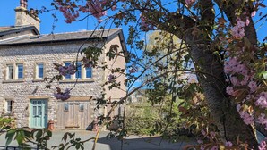 A stone building with a green door and windows, surrounded by trees and flowers.