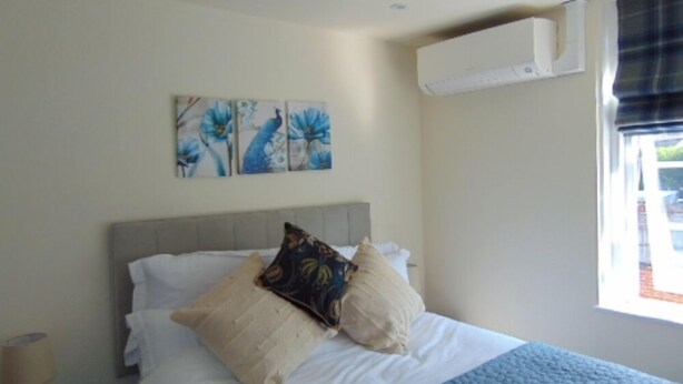 A bedroom with a bed, a nightstand, a wall-mounted air conditioner, and a window with curtains. - The Three Crowns (Loughborough)