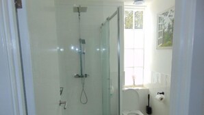 A bathroom with a glass-enclosed shower, a toilet, and a window with a view of greenery. - The Three Crowns (Loughborough)