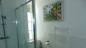 A bathroom with a glass shower enclosure, a toilet, a radiator, and a window with a view of greenery. - The Three Crowns (Loughborough)