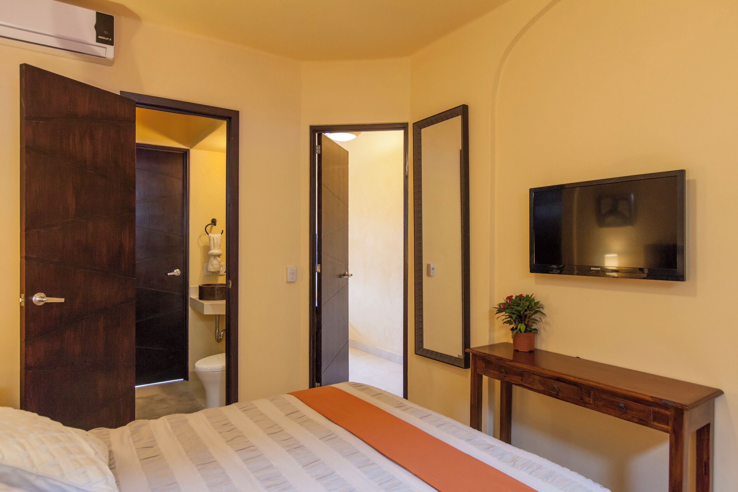 A hotel room with a bed, a bedside table, a mirror, and a television.