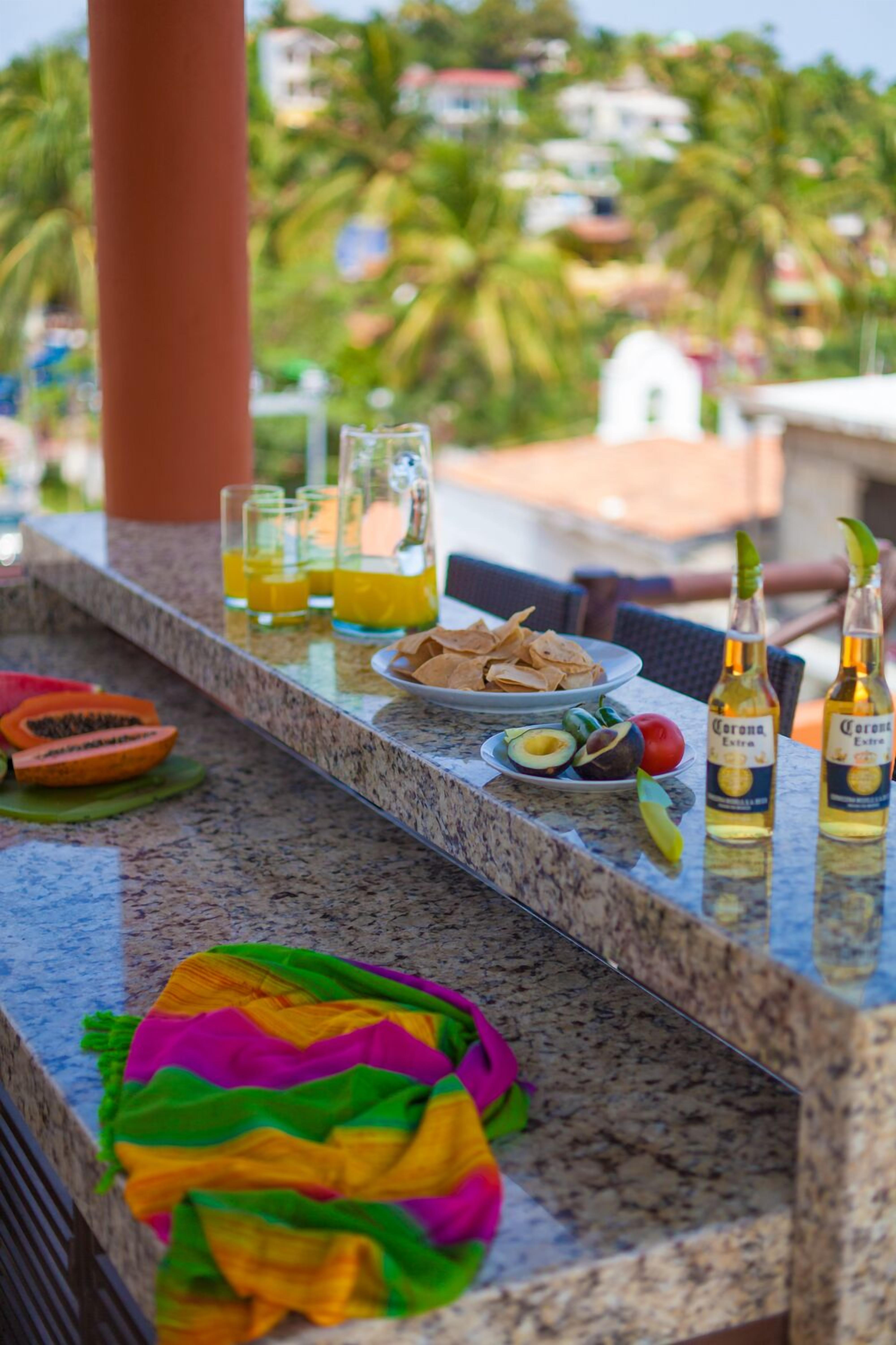 A bar area with drinks, snacks, and a colorful bag on a granite countertop.