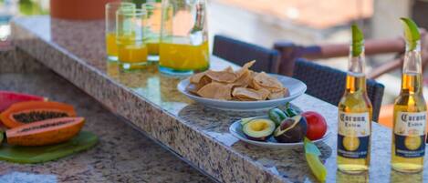 A bar area with drinks, snacks, and a colorful bag on a granite countertop.