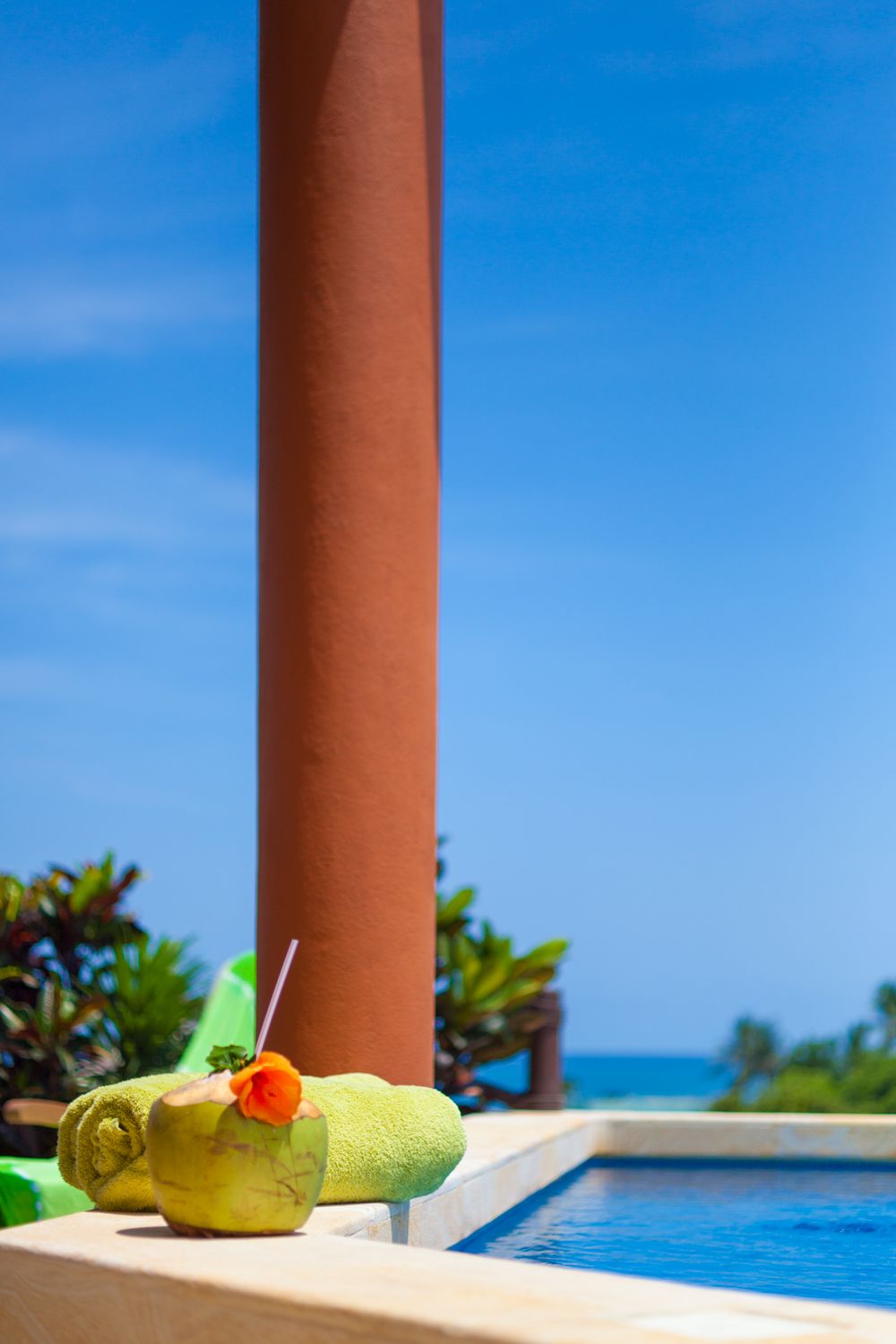 A poolside setting with a clear view of the ocean, a towel, and a cocktail in a coconut shell.