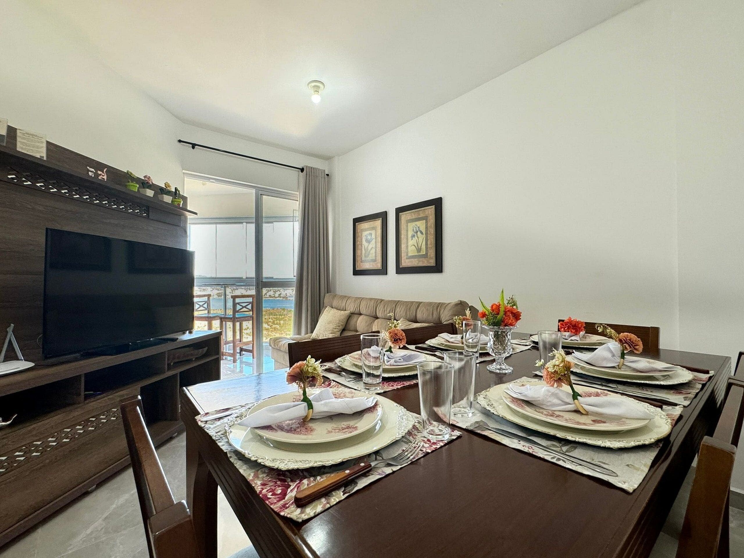 Comedor con una mesa grande dispuesta para cuatro personas, un televisor y un sofá.