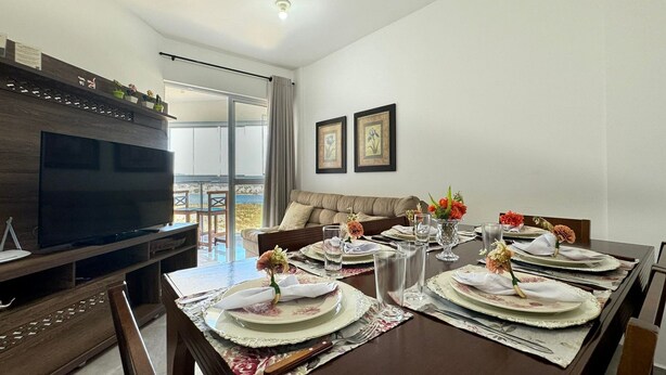 Comedor con una mesa grande dispuesta para cuatro personas, un televisor y un sofá.