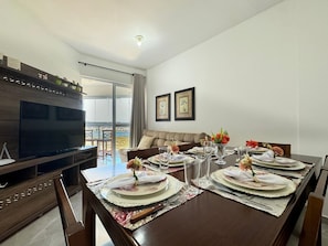 Comedor con una mesa grande dispuesta para cuatro personas, un televisor y un sofá.