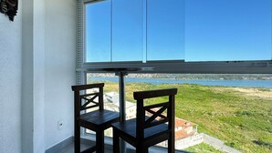 Un balcón con dos sillas de madera, una ventana que da a una masa de agua y vegetación.
