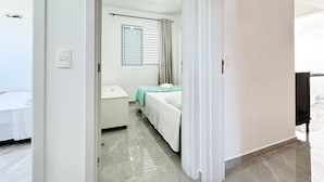 A hotel room with a bed, a bedside table, a window with curtains, and a bathroom with a toilet and sink.