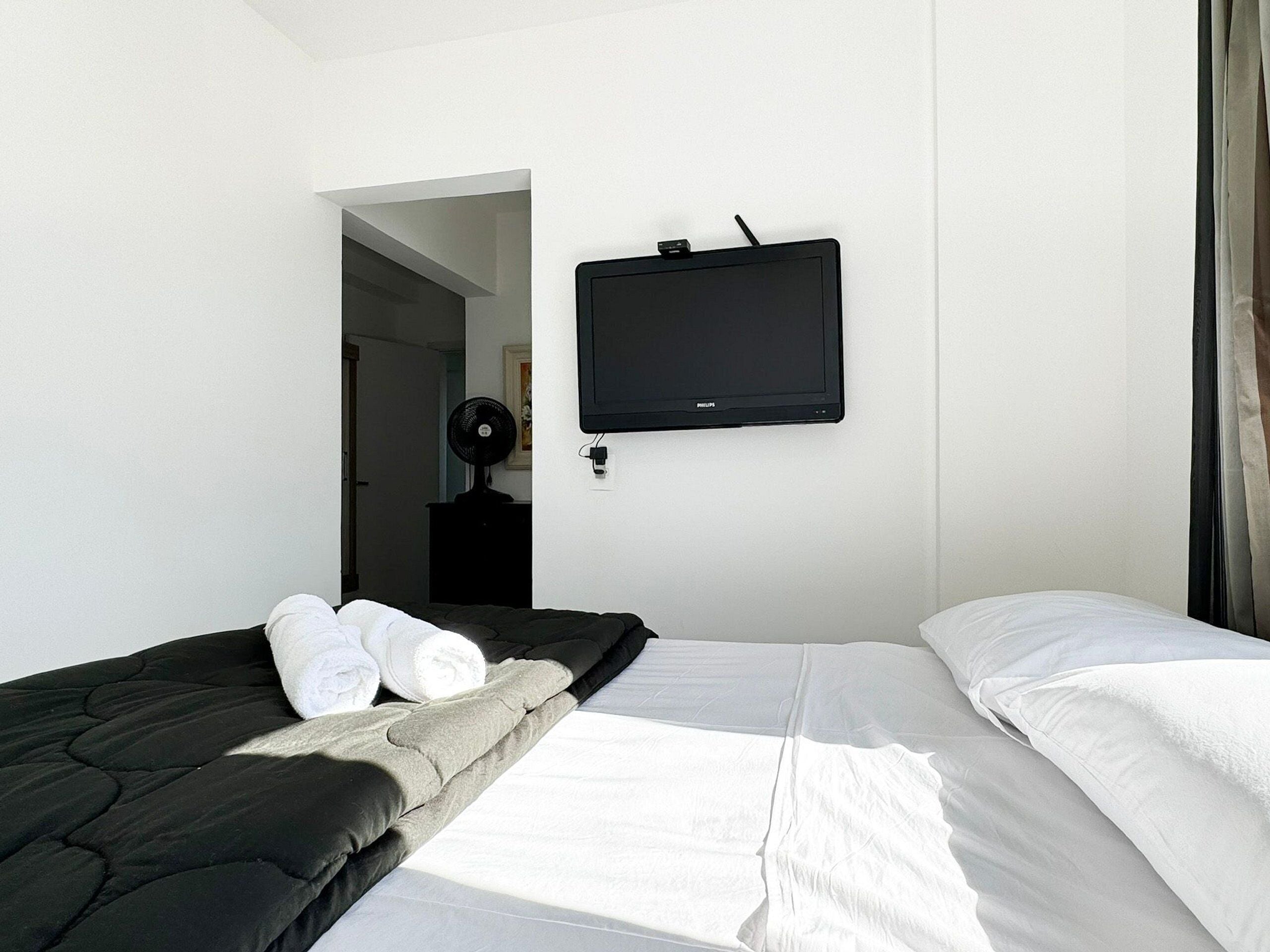Quarto de hotel com cama, televisão de tela plana na parede e ventilador.