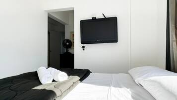 Quarto de hotel com cama, televisão de tela plana na parede e ventilador.