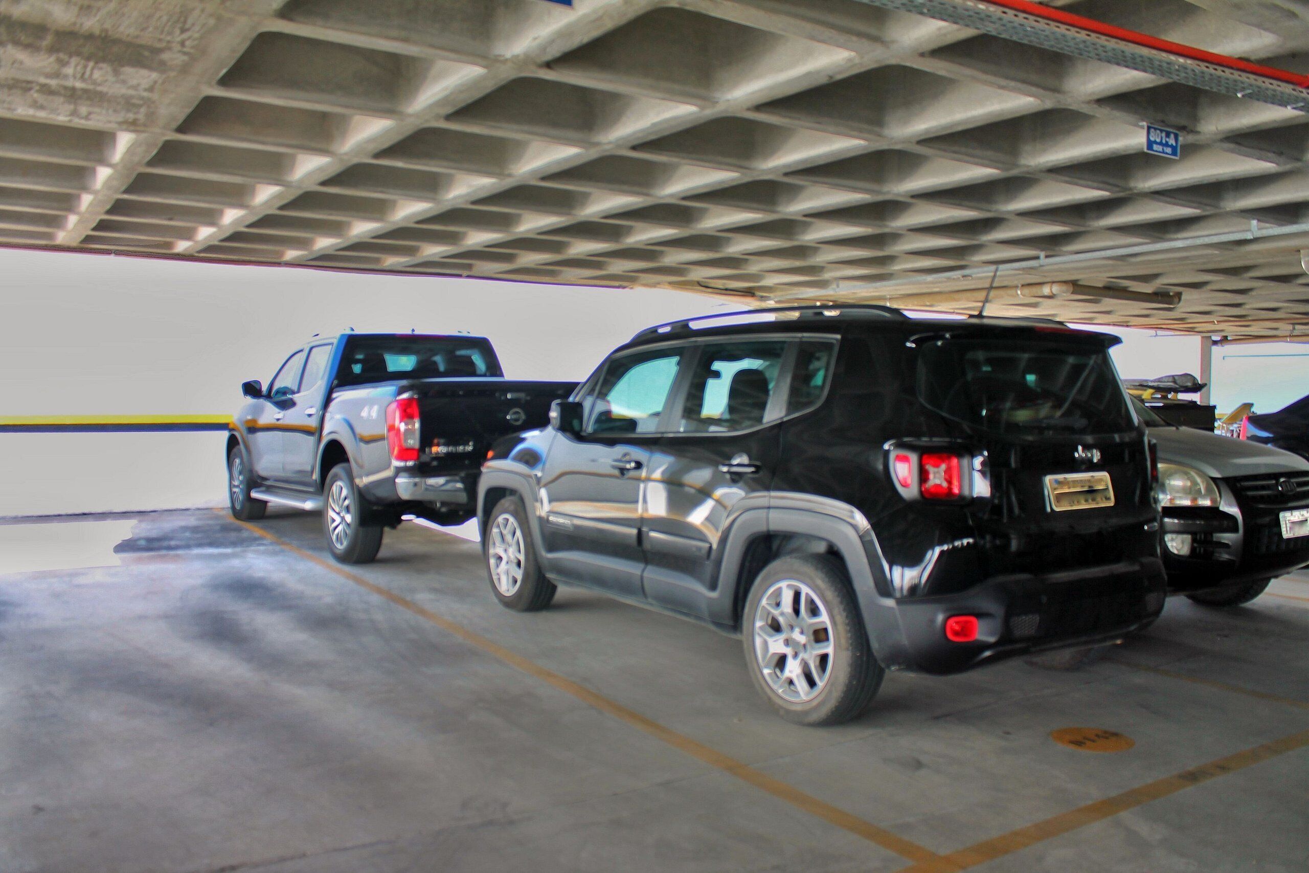 Un estacionamiento con vehículos, incluyendo un SUV negro y una camioneta.