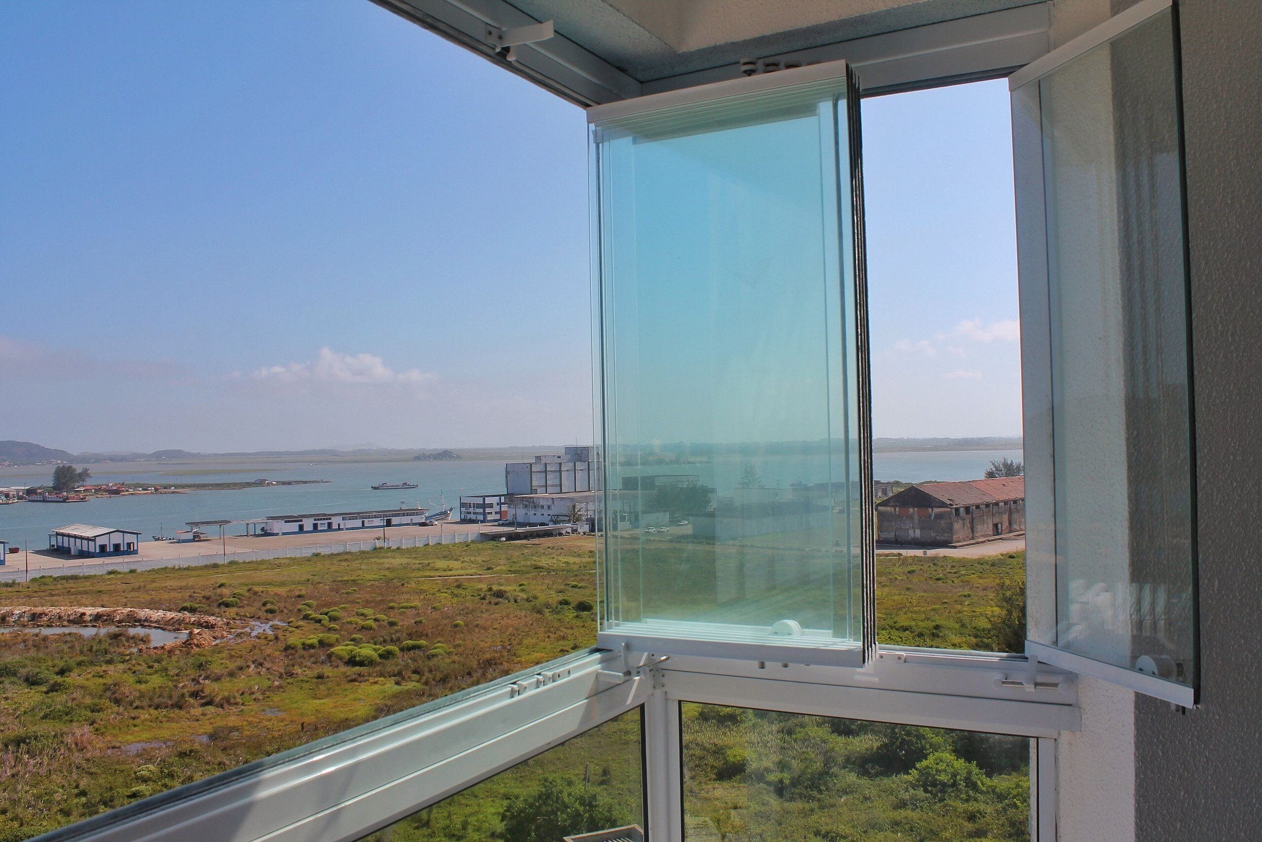 Janela com vista ampla da área costeira, incluindo um corpo d'água, edifícios e vegetação.