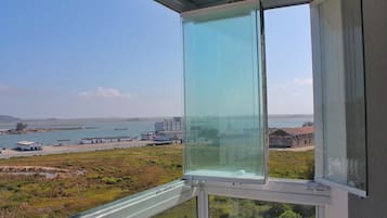 Janela com vista ampla da área costeira, incluindo um corpo d'água, edifícios e vegetação.