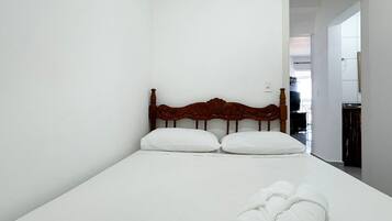 A small, neatly made bed with a wooden headboard in a minimalistic room.