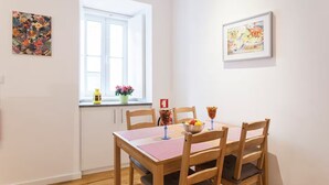 Ein Essbereich mit Tisch für zwei Personen, Holzstühlen, einem Fenster mit Vorhängen und zwei gerahmten Kunstwerken an den Wänden.