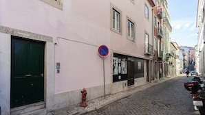 Eine enge Kopfsteinpflasterstraße mit einem rosafarbenen Gebäude, einer grünen Tür, einem roten Feuerhydranten und einem Verbotsschild für Parkplätze.