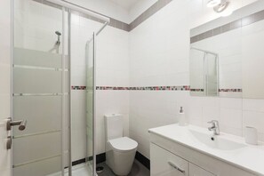 A modern bathroom with a glass shower enclosure, a toilet, and a sink with a mirror above. - Charming City Center (Lisbon)