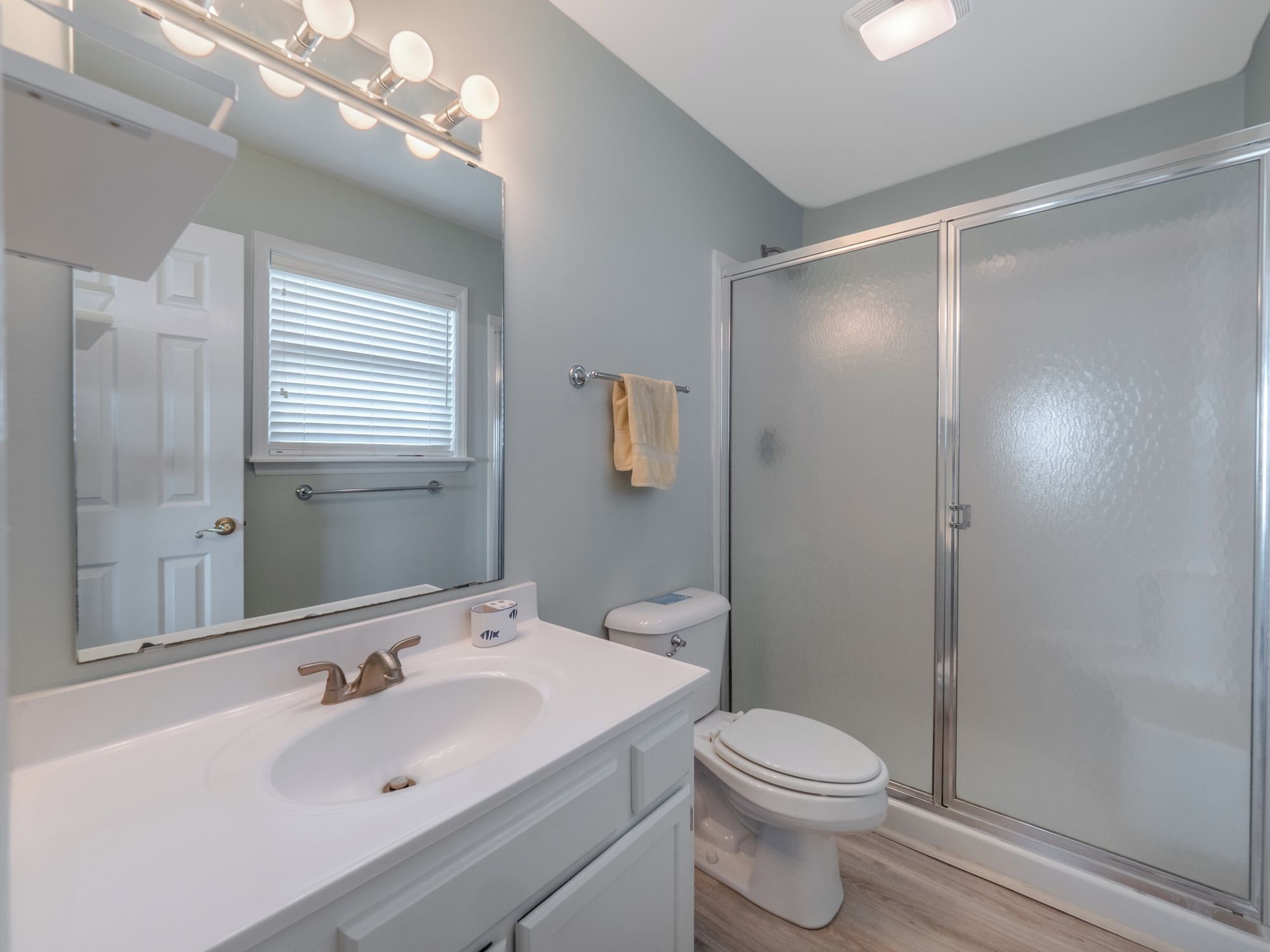 Une salle de bain avec un lavabo blanc, un miroir et des toilettes. Il y a un espace douche avec une porte en verre.
