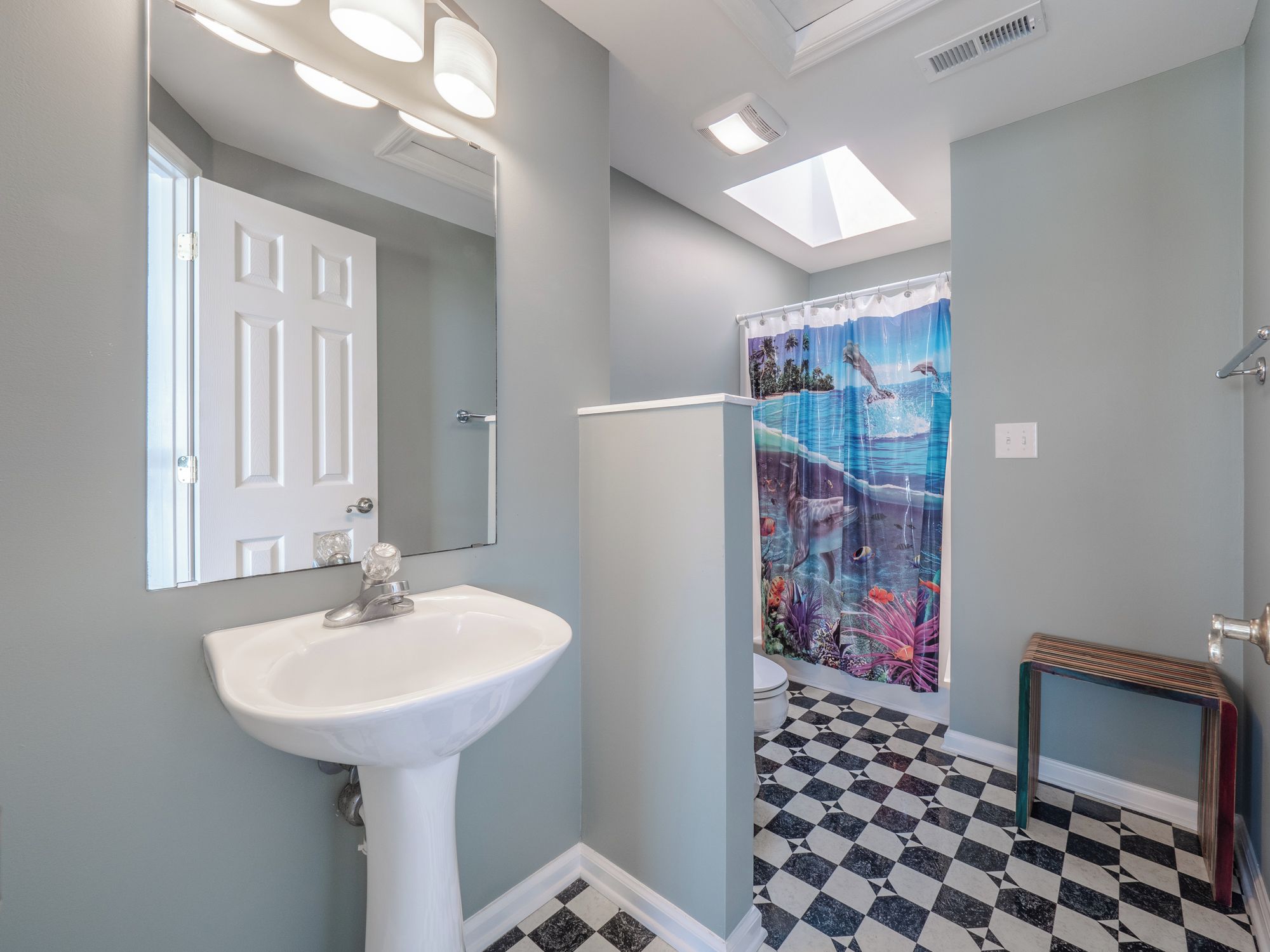 A bathroom with a white sink, a shower curtain with a marine theme, and a checkered floor.