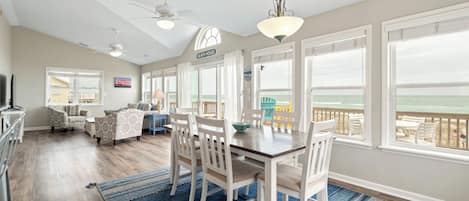 A spacious living room with a dining area, large windows, and a view of the ocean.
