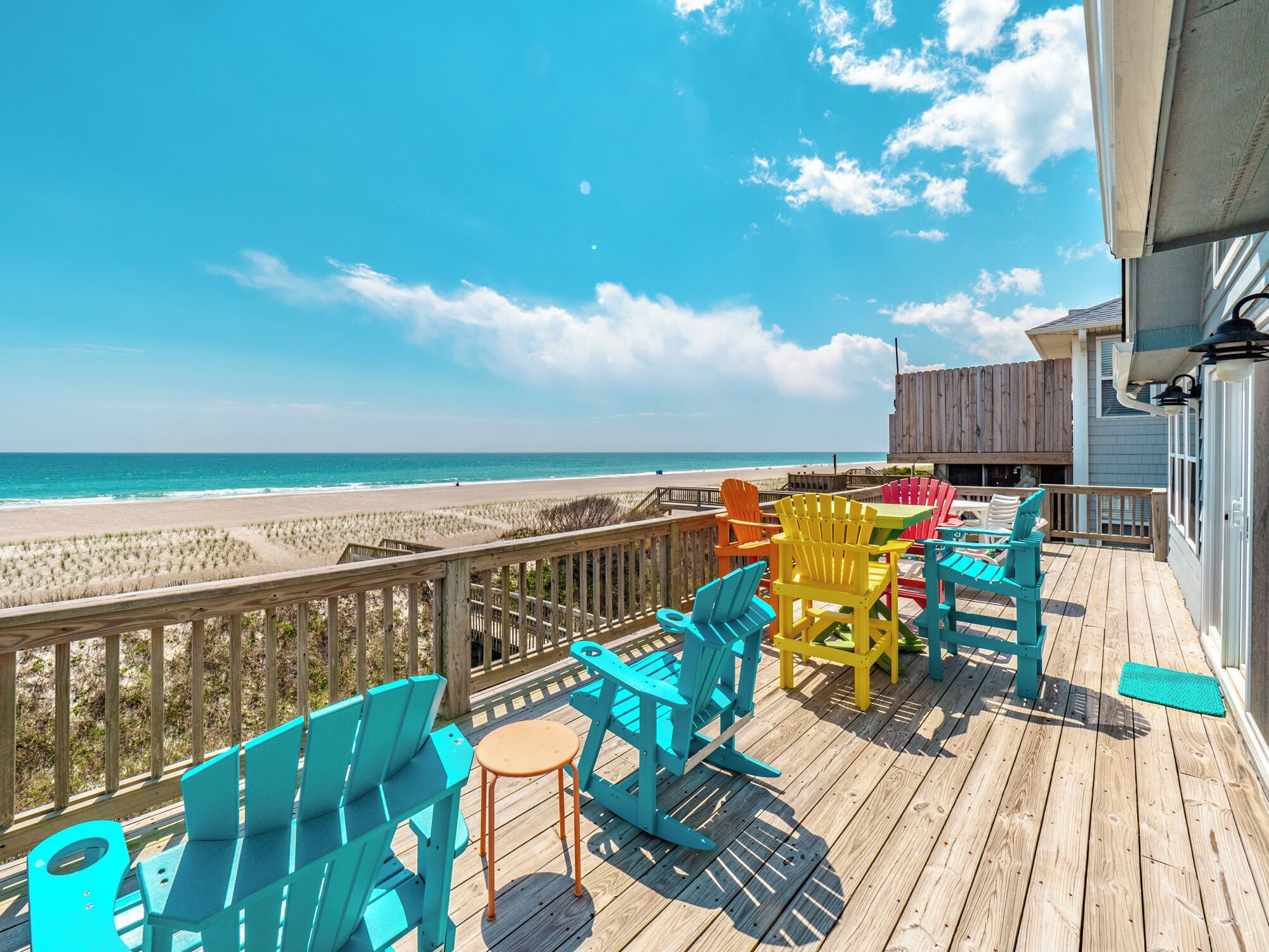 A wooden deck with colorful Adirondack chairs overlooking a beach.