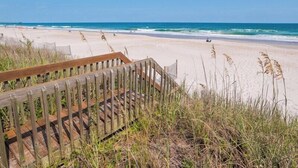 A wooden boardwalk leading to a sandy beach with waves in the background. - Costic by Topsail Realty (Holly Ridge)