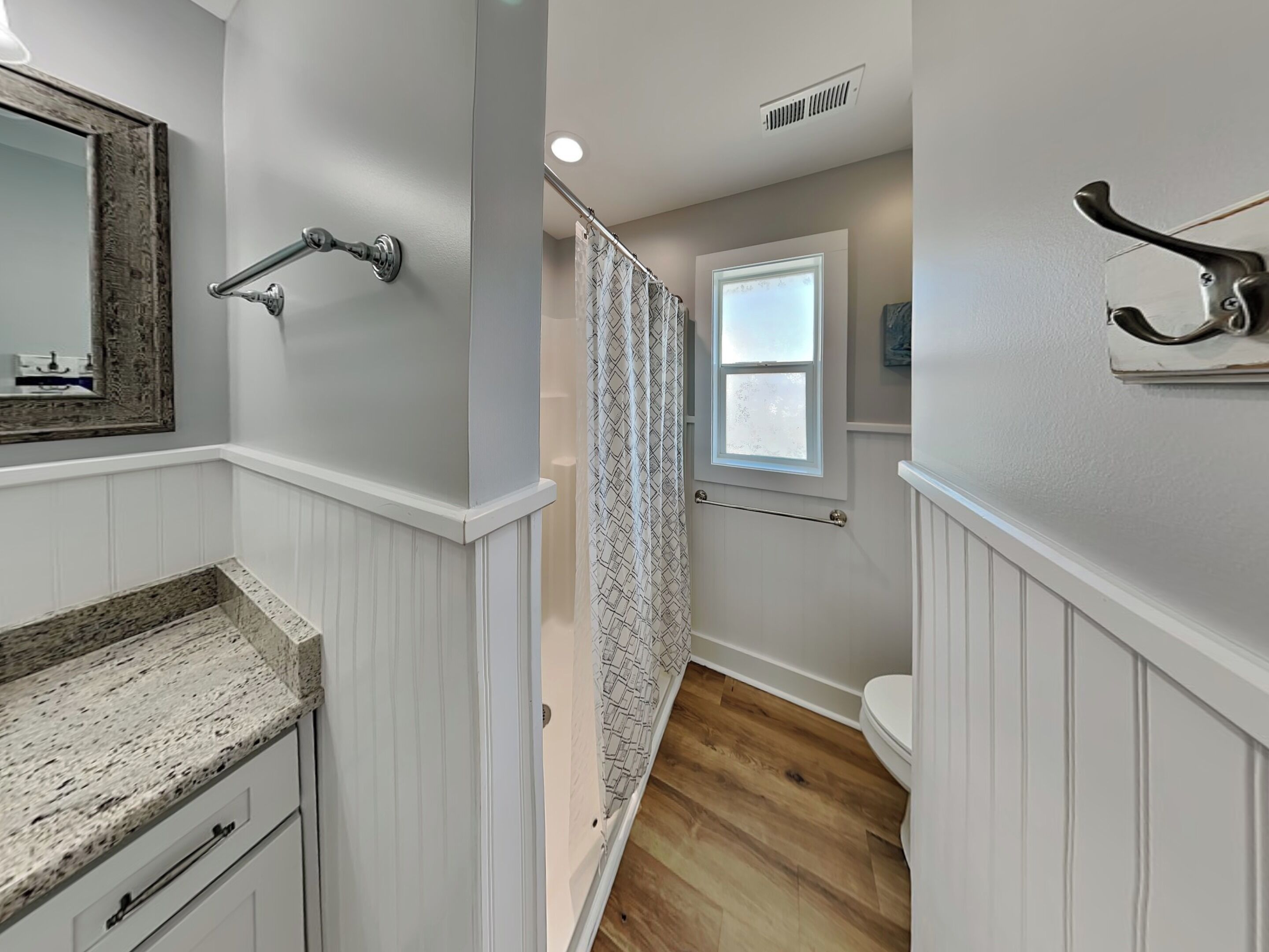 A bathroom with a wooden vanity, a shower curtain, a window, and a towel rack.