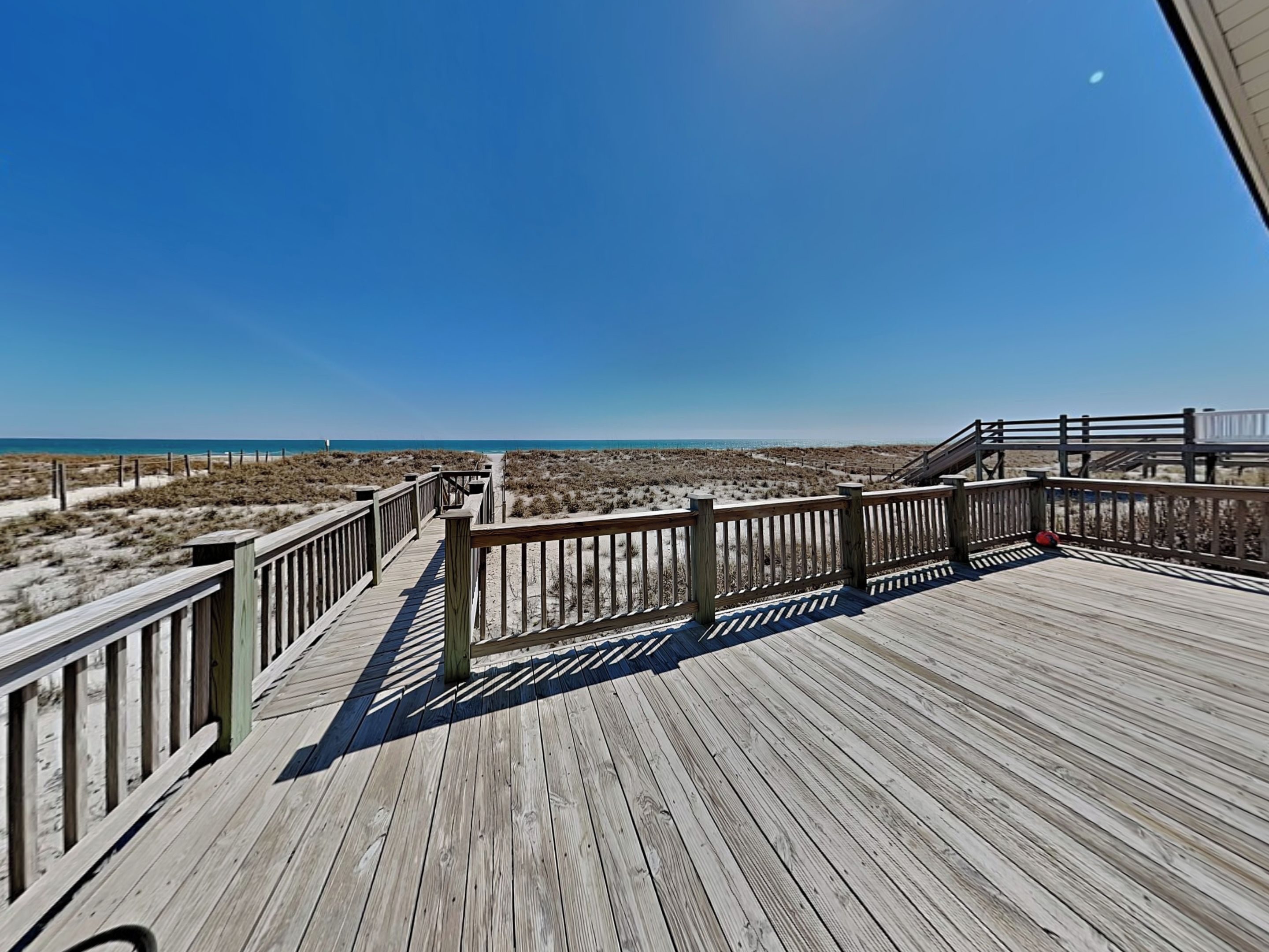 Ein hölzerner Steg führt zu einem Strand mit blauem Himmel.