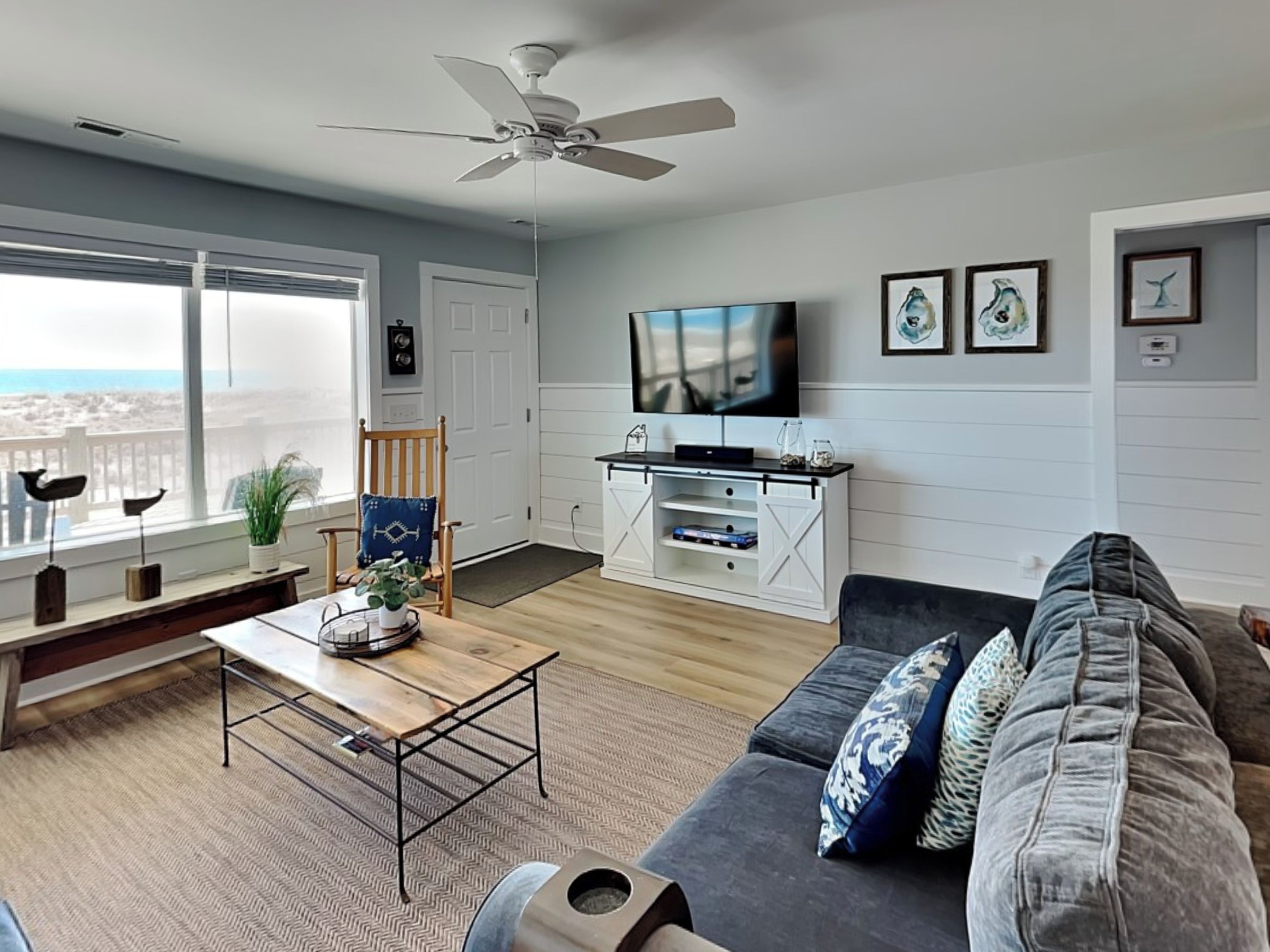 A living room with a large window, a ceiling fan, a TV, and a sofa.