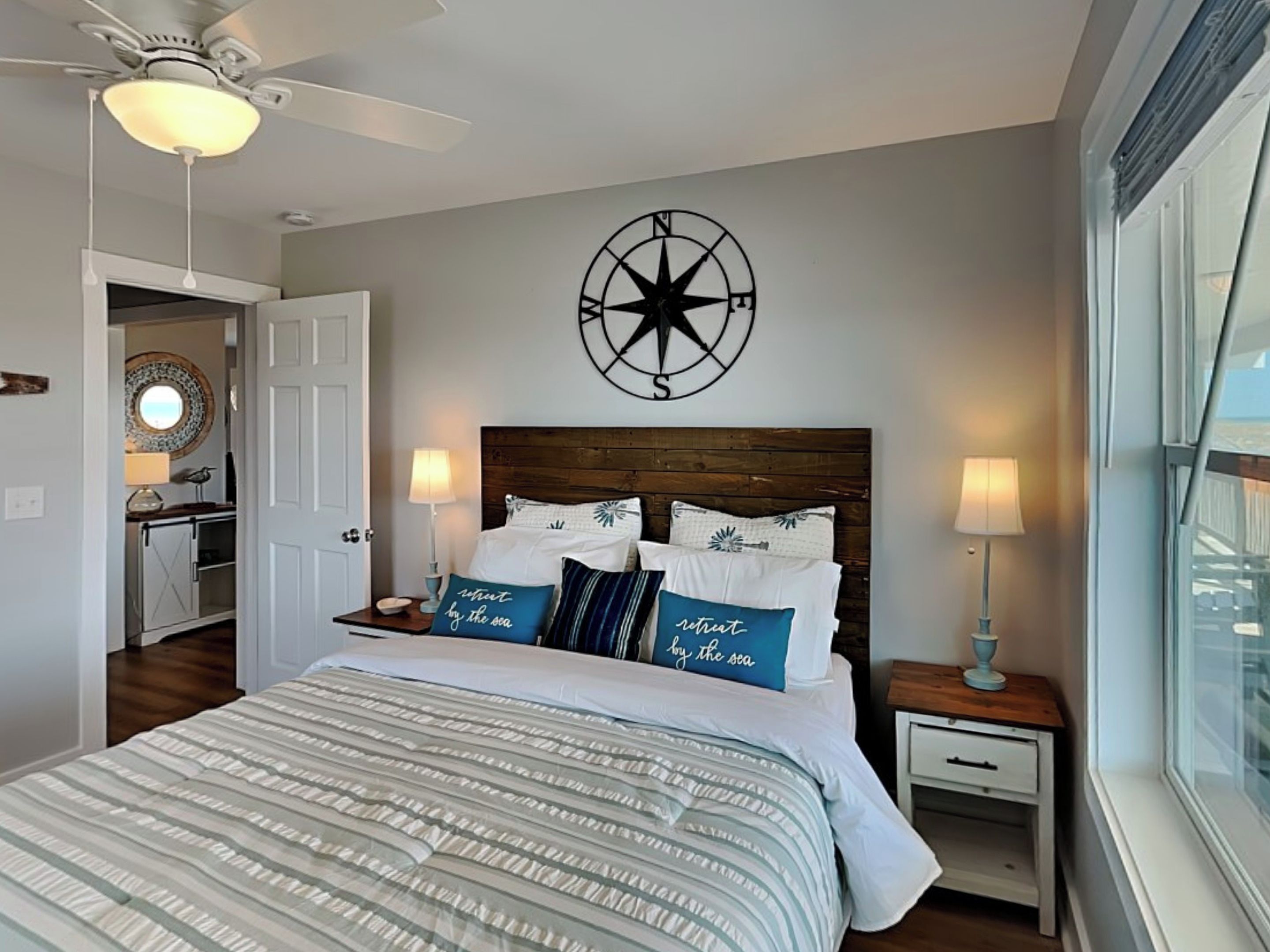 A bedroom with a bed, two bedside tables, a ceiling fan, a wall clock, and a window.