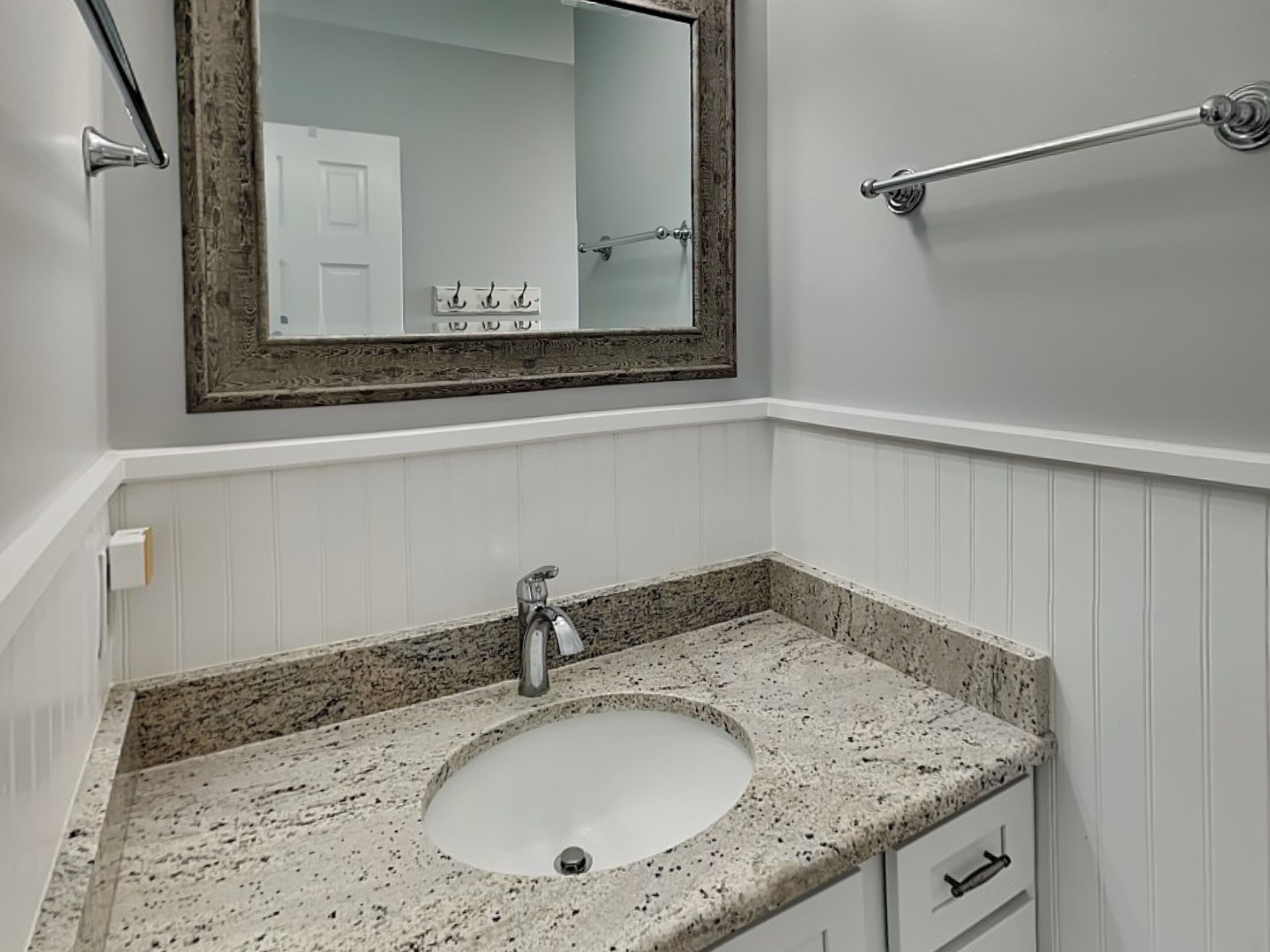 Un baño con lavamanos de encimera de granito, un espejo grande y un perchero para toallas.