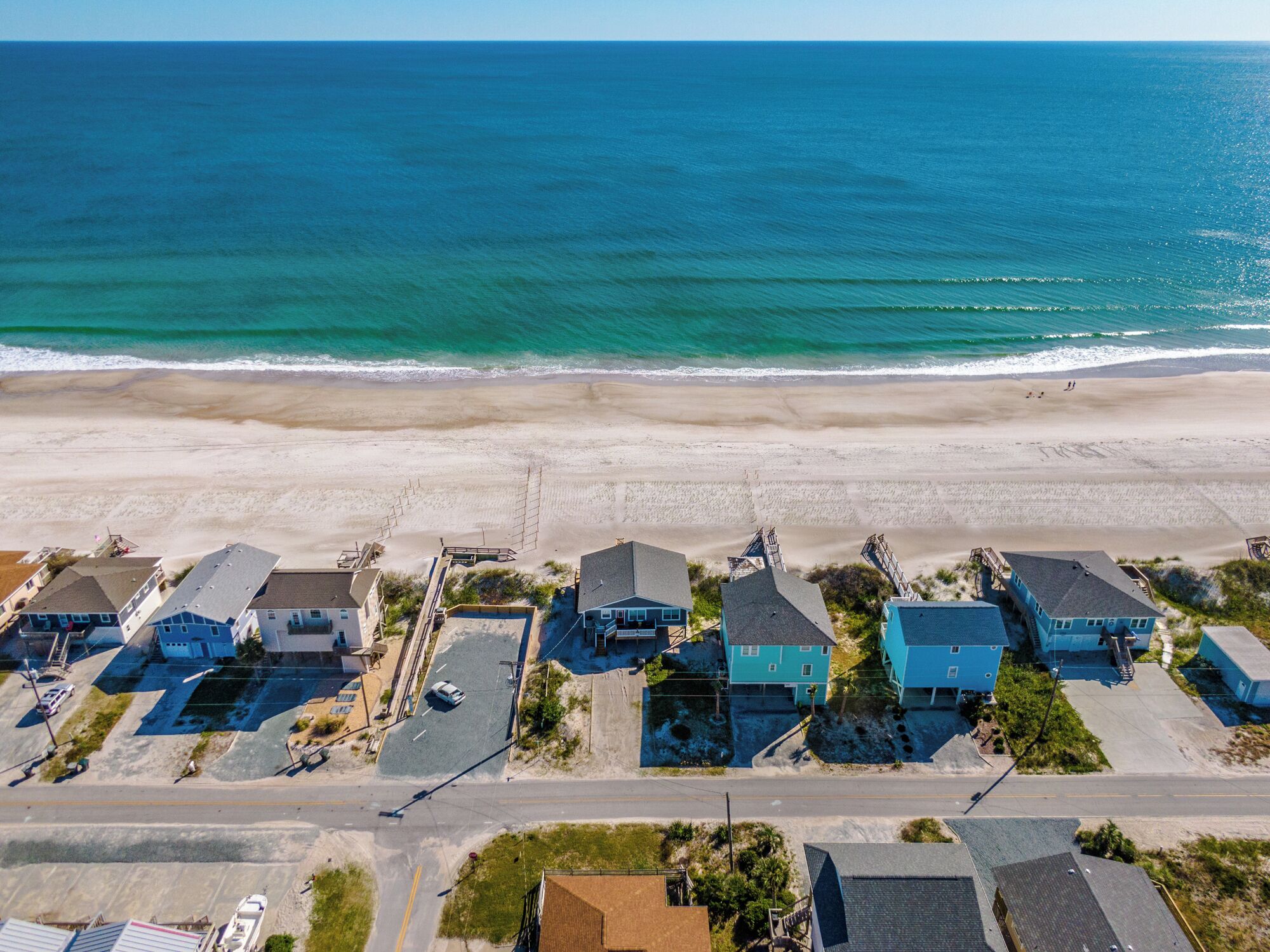 An aerial view of a coastal residential area with houses along the beach, a clear sky, and the ocean in the background.
