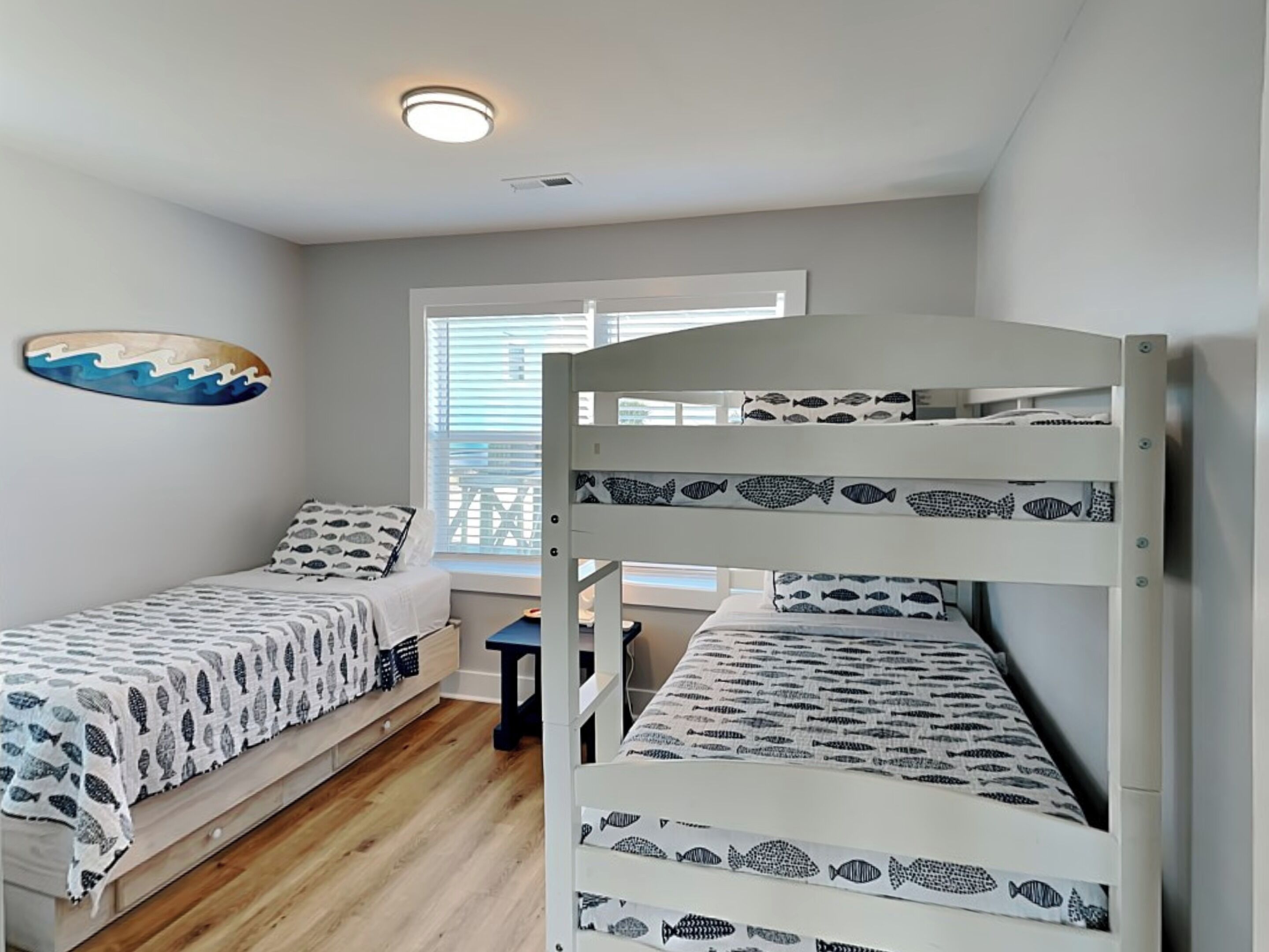 A bedroom with two bunk beds, a window with blinds, a ceiling light, and a wall decoration.