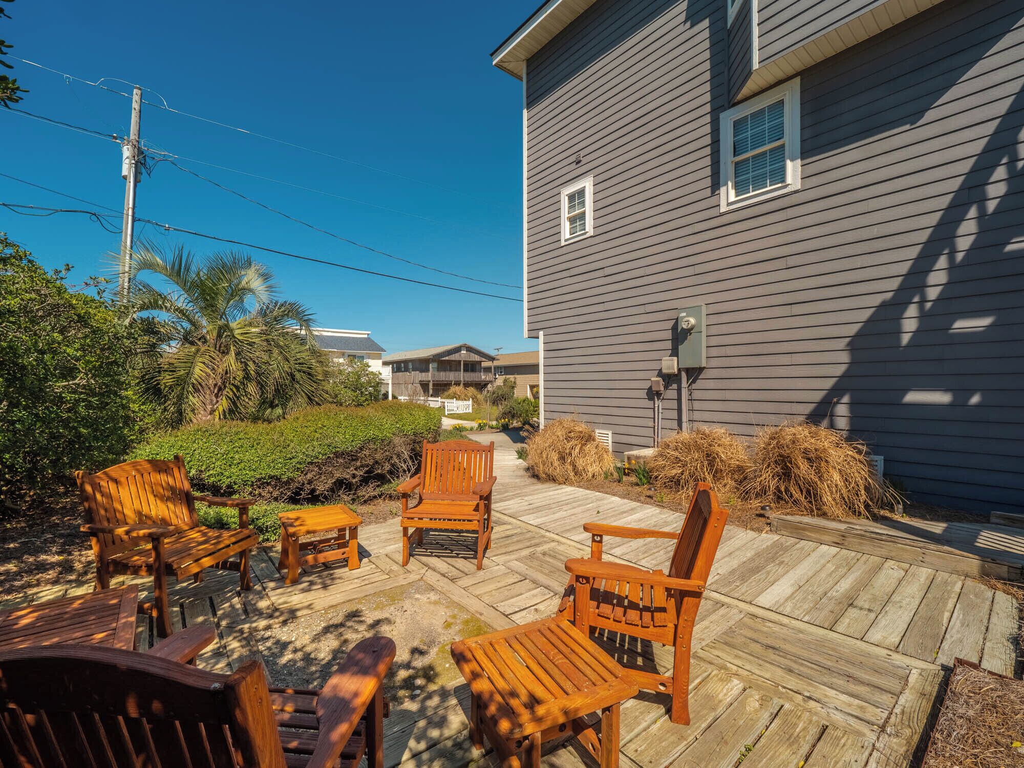 A wooden deck with outdoor furniture, a grey house, and a clear blue sky.