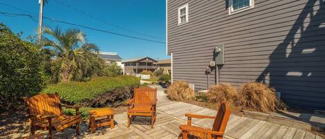 A wooden deck with outdoor furniture, a grey house, and a clear blue sky.
