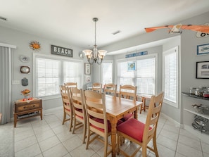 A dining area with a wooden table and chairs, a chandelier, and a sign that reads "BEACH". - Serendipity by Topsail Realty (Holly Ridge)