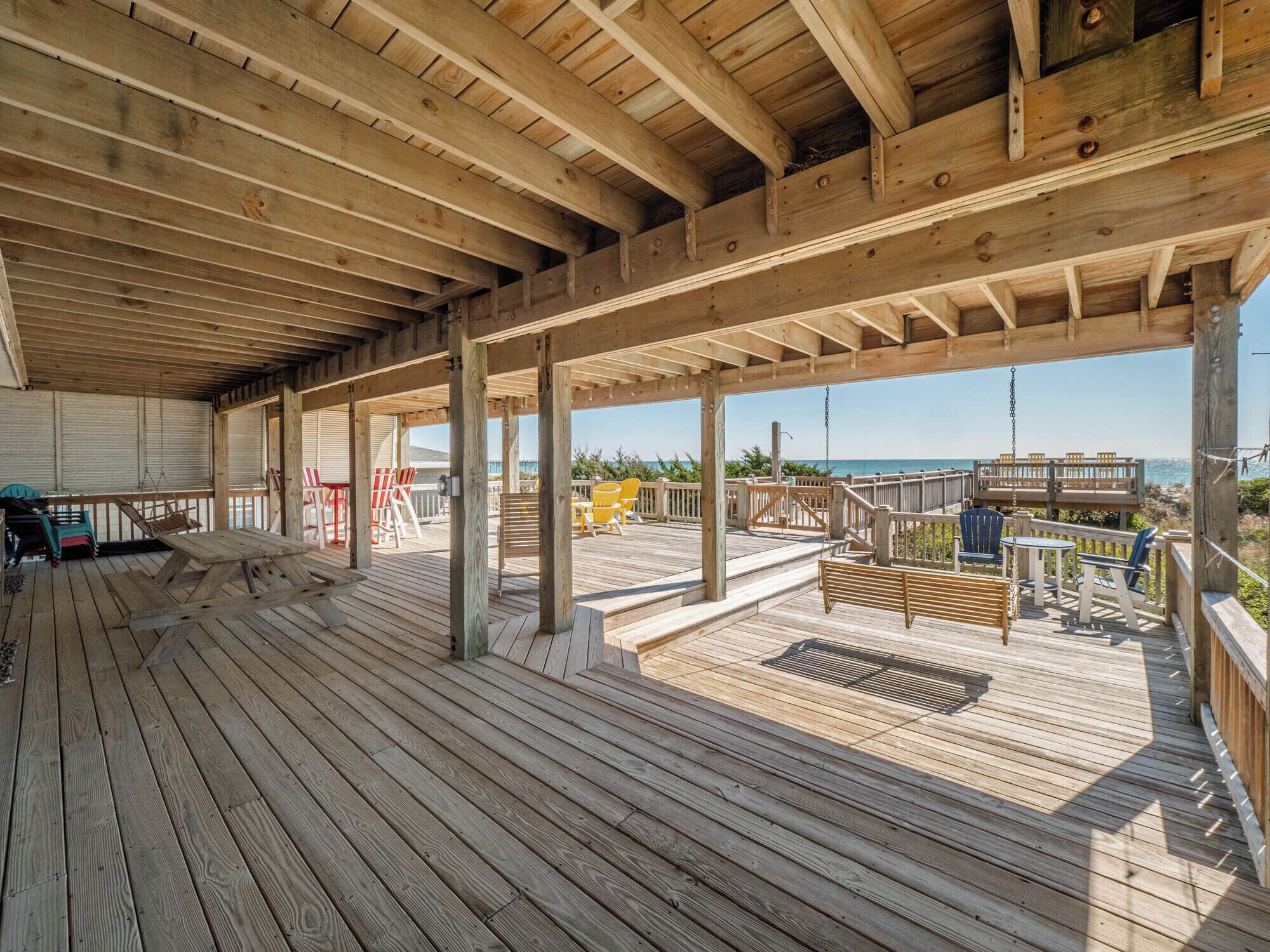 A wooden deck with a view of the ocean, outdoor seating, and a covered area.